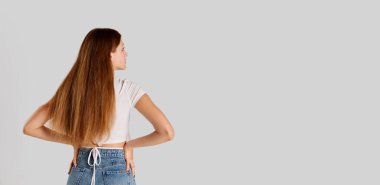 Gri stüdyo arka planında izole edilmiş, uzun saçlı, günlük kıyafetlerle poz veren genç bir kızın arka plan portresi. El ilanı. Duyguların kavramı, yaşam tarzı, yüz ifadesi, güzellik