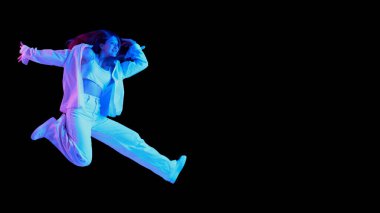 Siyah arka planda mavi ışıkta izole edilmiş beyaz gündelik kıyafetlerle poz veren güzel bir kızın portresi. Atlıyorum. Duyguların kavramı, yaşam tarzı, yüz ifadesi, güzellik, moda, gençlik