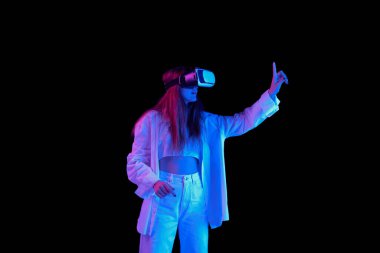 VR gözlükleriyle poz veren güzel bir kızın portresi siyah arka planda mavi neon ışıkta izole edilmiş. Duyguların kavramı, modern teknolojiler, yaşam tarzı, yüz ifadesi, güzellik, moda, gençlik