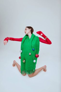 Gri arka planda izole edilmiş süslemeleri olan büyük yeşil eşarp takan güzel bir kızın portresi. Noel tarzı. Eski moda kavramı, sanat fotoğrafçılığı, stil, nonoş, güzellik, reklam.