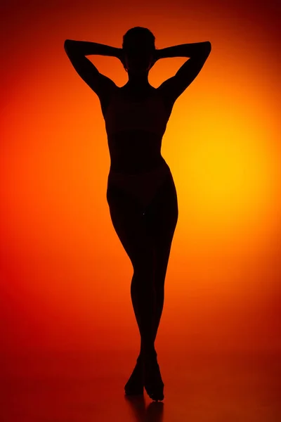 Silhouette of female full-length body isolated over orange background. Relaxation, wellness. Body art, aesthetics. Concept of beauty, femininity, health, sport, lifestyle