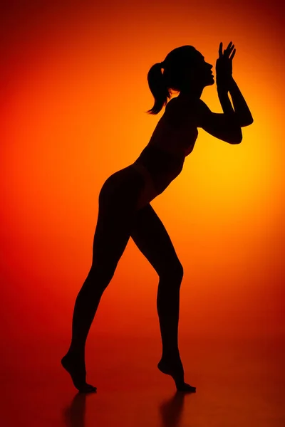 Silhouette of female full-length body isolated over orange background. tender movements. Body art, aesthetics. Concept of beauty, femininity, health, sport, lifestyle