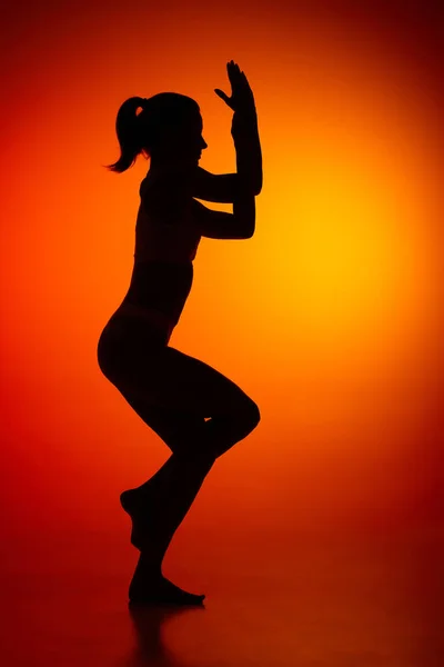 Silhouette of female full-length body isolated over orange background. Well coordinated movements. Body art, aesthetics. Concept of beauty, femininity, health, sport, lifestyle