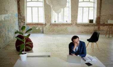 Boş bir odada dizüstü bilgisayarla masada düşünceli bir yüzle oturan genç iş adamının portresi. Proje başarısızlığı, profesyonel kriz. İş kavramı, zorluklar, iş, meslek