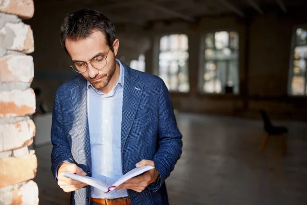 Portrait of businessman standing at the wall in empty room, making notes, working on new company opening. Concept of business, challenges, work, occupation, brainstorming, company development