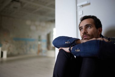 Boş bir odada oturan genç iş adamının portresi. İş kapanışı. Depresyon ve kriz. Kariyer başarısızlığı. İş kavramı, zorluklar, iş, meslek, duygusal stres