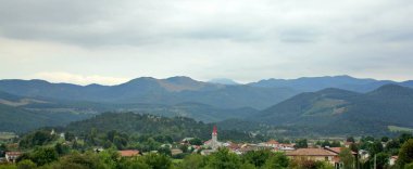 Önlerinde dağlar, tarlalar ve çayırlar, Slovenya manzarası, yeşil çayırlar, düz dağlar ve hafif bulutlu gökyüzü.