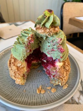 Fıstık aromalı kremalı bir tabakta şekerli puf, içinde krema ve ahududu reçeli, tabakta tatlı tatlı, buğulanmış kek, şekerli puf böreği