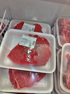 beef steak on a plastic tray, steak wrapped under foil in a store refrigerator, piece of beef sold in a store