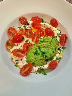 Büyük bir tabak krem peynirli zeytinyağı, dilimlenmiş avokado, ikiye bölünmüş domates, sağlıklı yiyecek, taze sebze ve süt ürünleri.