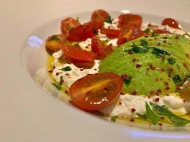 Büyük bir tabak krem peynirli zeytinyağı, dilimlenmiş avokado, ikiye bölünmüş domates, sağlıklı yiyecek, taze sebze ve süt ürünleri.