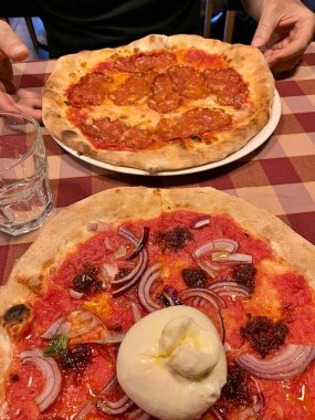 İtalyan pizzacısı, masada iki çeşit pizza, bufala mozzarella soslu pizza, schiacciata salamlı pizza, klasik İtalyan restoranı, kırmızı kareli masa örtüsü.