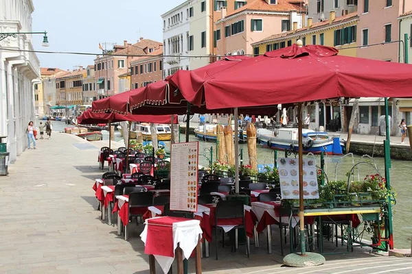 Küçük bir Venedik sokağı, Venedik 'teki su kanalının yanındaki restoranlar, kanal kenarındaki restoranlar, restoran masalarının üzerindeki şemsiyeler.