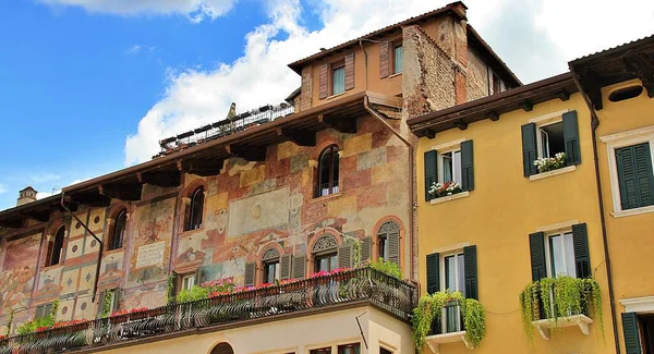 Italian architecture, Verona architecture, blue sky with white clouds, wooden shutters and greenery on balconies, paintings on the facade of a tenement house