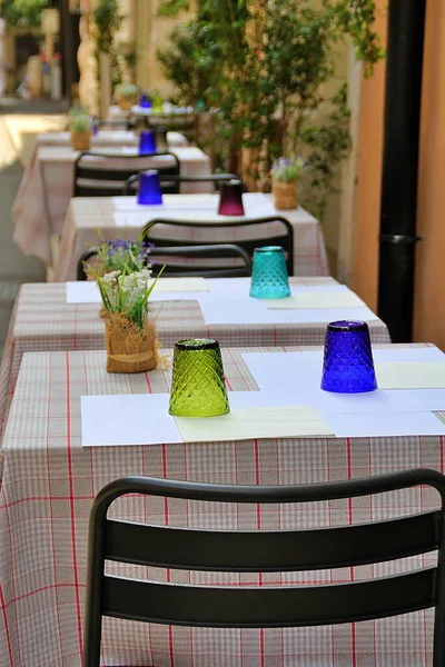 restaurant tables covered with tablecloths, outdoor tables in front of the restaurant, colored glasses on restaurant tables, outdoor tableware, summer tables