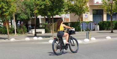 cycling girl, electric bicycle, fast riding person on a big black bicycle, cyclist in the city, street with trees 