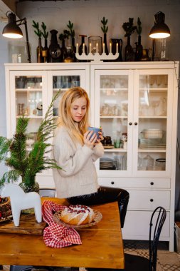 Yeni yıl süslemeleri için mutfakta çay içen güzel sarışın bir kadın..
