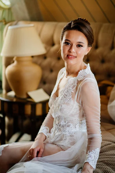 Uma noiva em um manto de renda sentada na cama. manhã antes do casamento. — Fotografia de Stock