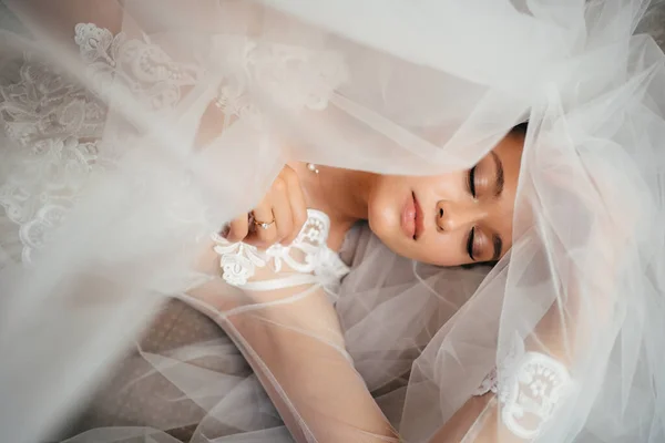 Eine Braut im Spitzengewand liegt auf einem Schleier im Bett. Morgen vor der Hochzeit. — Stockfoto