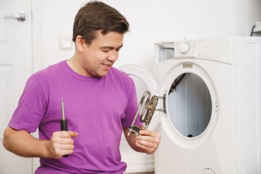 Çamaşır makinesinin tamircisinde eski borular elektrikli ısıtıcı ve tornavida var.