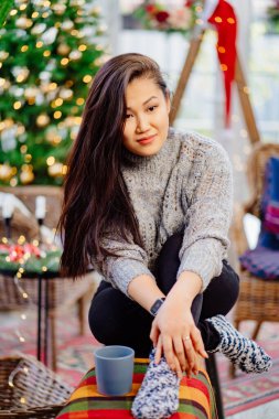 Oturma odasında yeni yıl için süslenmiş bir fincan çayla güzel bir kadın.