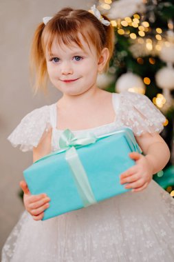 Noel ağacında elinde hediyeyle beyaz elbiseli mutlu bir kız.. 