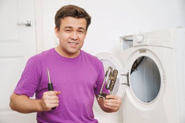 Çamaşır makinesinin tamircisinde eski borular elektrikli ısıtıcı ve tornavida var.