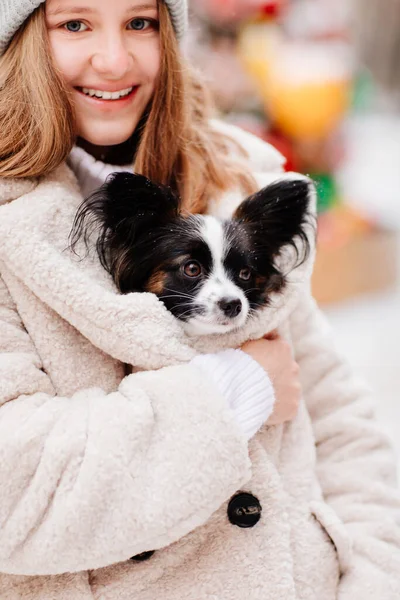 아름답고 행복 한 아가씨 가 코트 안에 있는 작은 개 양귀비를 따뜻하게 해준다. — 스톡 사진