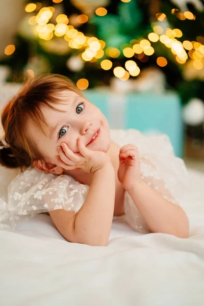 Uma menina bonito encontra-se sob a árvore de Natal. feliz ano novo. — Fotografia de Stock