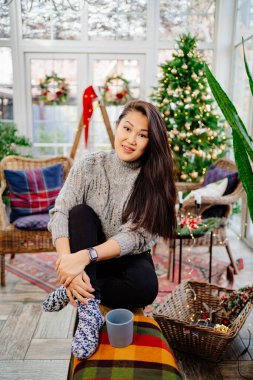 Oturma odasında yeni yıl için süslenmiş bir fincan çayla güzel bir kadın.