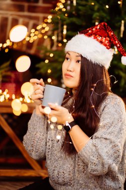 Güzel bir Koreli esmer Noel Baba şapkasıyla kakao içiyor. 