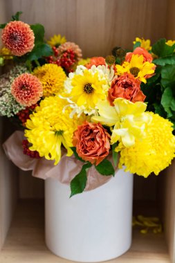 Dolabın rafındaki bir şapka kutusunda sarı ve turuncu bir çiçek buketi.. 