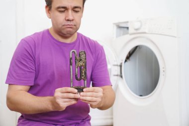 Çamaşır makinesinin tamircisi eski boru elektrikli ısıtıcıyı tutuyor. 
