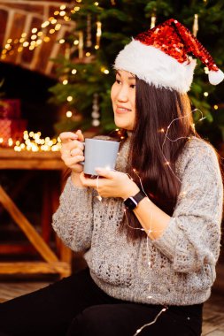 Güzel bir Koreli esmer Noel Baba şapkasıyla kakao içiyor. 