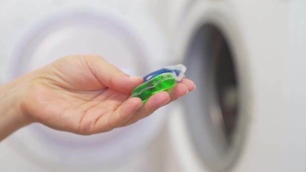 Uma mulher segura na cápsula da mão com detergente para a máquina de lavar roupa. — Vídeo de Stock