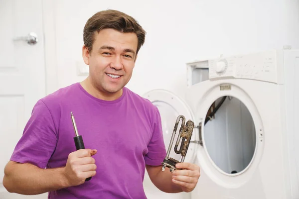 Reparador de lavadora sostiene viejo calentador eléctrico tubular y destornillador — Foto de Stock