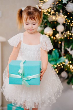 Noel ağacında elinde hediyeyle beyaz elbiseli mutlu bir kız.. 