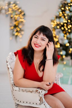 Noel ağacının arka planında kırmızı elbiseli çekici, tombul kadın.