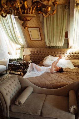 Dantel bornozlu bir gelin yatakta yatıyor. Düğünden önce sabah.
