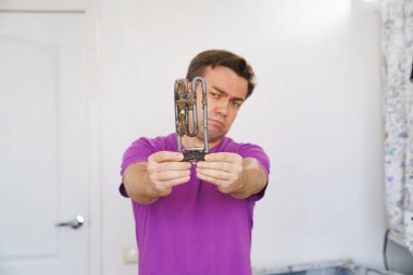 Çamaşır makinesinin üzgün tamircisi eski borulu elektrikli ısıtıcıyı tutuyor. 