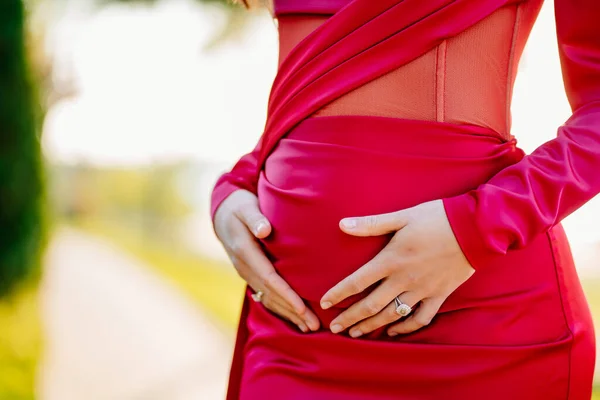 Беременная женщина в красном обтягивающем платье гладит животик руками. — стоковое фото