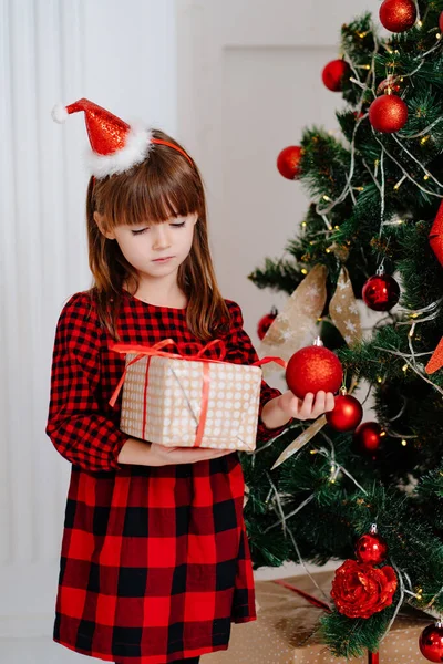 Menina bonito em um vestido xadrez vermelho e um boné com um presente na mão — Fotografia de Stock