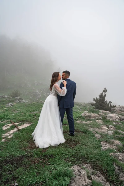 Νεόνυμφοι αγκαλιάζονται σε ομιχλώδες ορεινό δάσος. γάμος στο ταξίδι — Φωτογραφία Αρχείου
