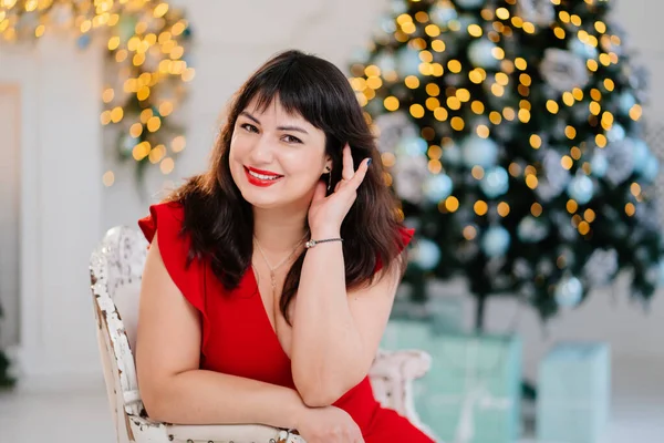 attractive plump woman in red dress against background of Christmas tree