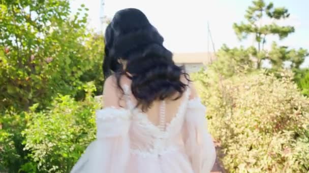 Uma bela noiva morena em um vestido longo andando ao longo do caminho no parque. — Vídeo de Stock
