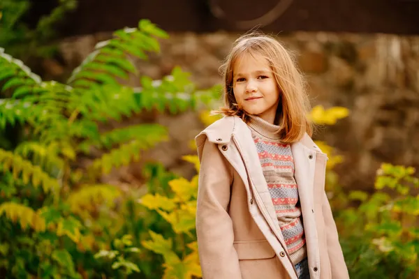 Une jolie petite fille en manteau et un jean dans un parc d'automne au feuillage jaunâtre. — Photo