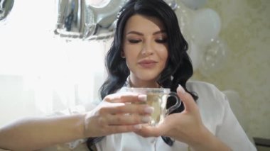 Kapat. Gelinin sabahı. Beyaz pijamalı güzel bir kadın çay içiyor..