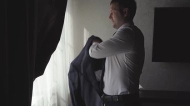 Bir adam pencerenin yanında bir ceket giyer. erkek modası. 
