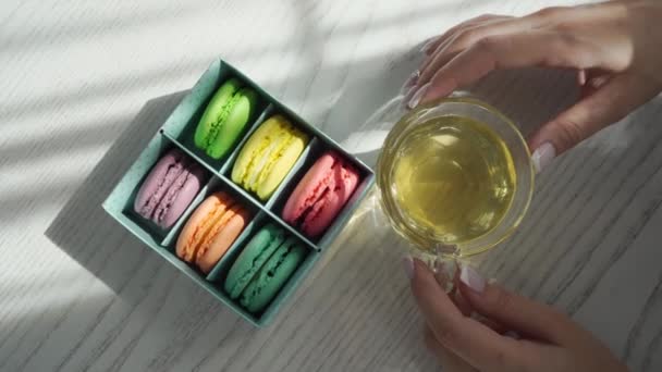 Vrouwenhanden houden een kopje groene thee vast en nemen macarons taarten. — Stockvideo