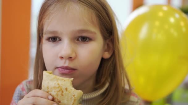 En liten flicka äter en uppstoppad pannkaka på ett café. traditionell rysk snabbmat. — Stockvideo